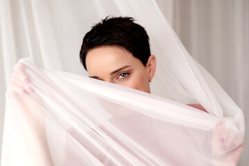 Attractive brunette woman flirts hiding her face behind transparent fabric