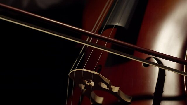 Artist plays with a bow on the strings of the cello in the darkness. Close-up musician plays with a bow of a violoncello.