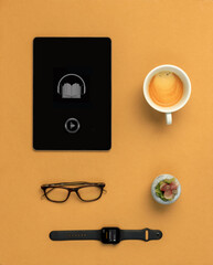 tablet with audiobook coffee reading glasses a plant and a smartwatch on a brown table
