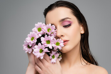 brunette young woman with pink eye shadows holding flowers isolated on grey