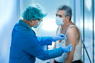 Dottore con tutte le protezioni mediche prepara una siringa con il vaccino che sta per iniettare ad...