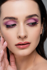 Fototapeta na wymiar close up of brunette woman with pink eye shadows looking away isolated on grey
