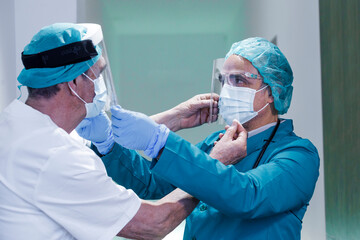 Coppia di medici si aiutano nella preparazione con tutte le protezioni prima di un intervento...