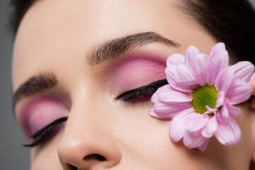 cropped view of sensual young woman with pink eye shadows holding flower