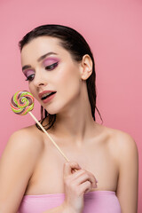 young woman with bare shoulders holding lollipop isolated on pink