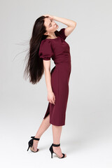 portrait of a beautiful girl 25 years old, European appearance, with dark long hair, in a red dress, on a light gray background in the studio. Portrait of a brunette, sideways