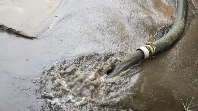 Close-up big pipe of power pump machine pouring mud sludge waste water with sand and silt on ground. Sand-wash and coast-depeening. Septic sewage maintenance service. spring flood deluge aftermath