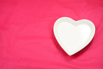 White heart, heart shaped plate-dish, light color heart-shaped plate. Dishes for food, for dinners, weddings or romantic moments. Pink background. Dinner ideas. Sign of romantic.   