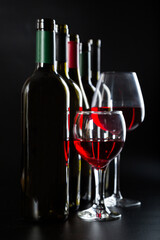 several different bottles of wine and a glass with red wine on a dark glossy background.