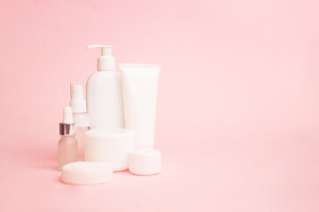 White jars of cosmetics on a pink pastel background. Bath accessories. Face and body care concept. Copy space.