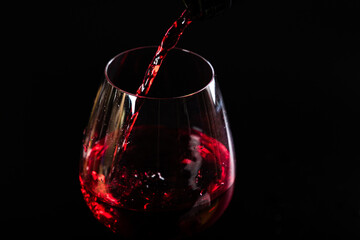 Naklejka na ściany i meble Pouring red wine with splashes and drops into a glass on a black background.