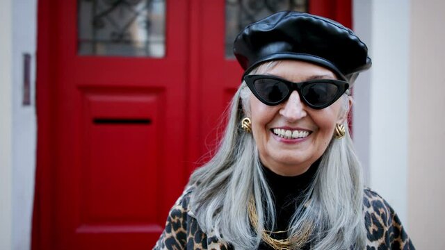 Senior chic woman with sunglasses standing outdoors, looking at camera.