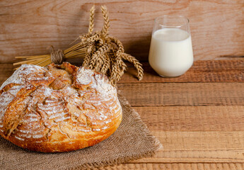 A loaf of bread made from wheat flour, a glass of milk on wooden boards.