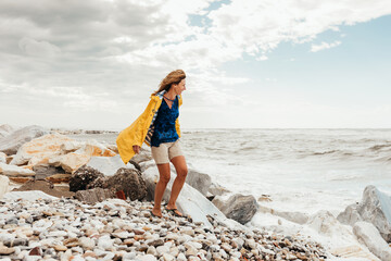 happy woman with blowing hair in a yellow raincoat looking at the ocean on a windy day