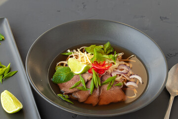 Asian soup Ramen served in black bowl on gray table