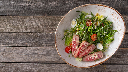 Fried tuna slices with arugula, tomatoes and eggs. Top view, text space