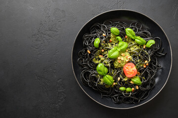 Black pasta spaghetti squid Ink with sauce Pesto in black bowl on black background. Top view.