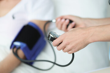 Doctor measures patient's blood pressure in bed closeup