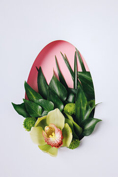 Beautiful Easter egg with green leaves and orchid spring flower on pink and bright white background. Minimal Easter holiday concept. Flat lay, top view.