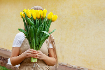 The girl hides her face behind a large bouquet of yellow tulips. Women's Day, Valentine's Day, Mother's Day.