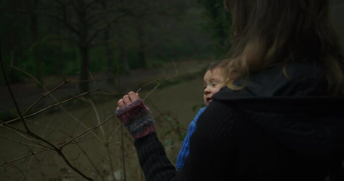 A young mother carrying her baby in a sling is looking at tree branches in the winter