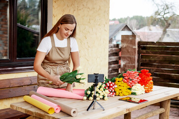 A young female florist packs bouquets of tulips in her shop and shoots a video master class for her blog. Women's Day and Valentine's Day