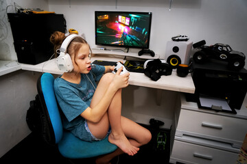 The girl plays computer games and holds a white game controller in her hands. © Aboltin