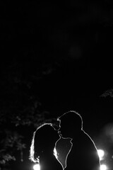 Young couple enjoying outdoors in the forest during night time. Silhouette picture of the couple at the forest with backlight. Kissing couple