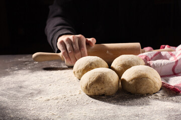 Homemade wholemeal dough for bread and female hand on wooden table with flour, rolling-pin, dark rustic background.