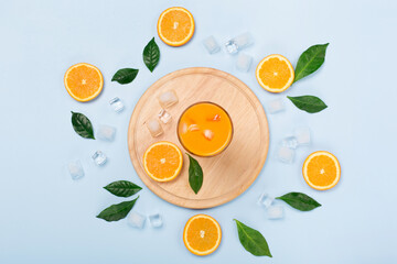 Fresh orange juice in glass with sliced oranges and ice on blue background.