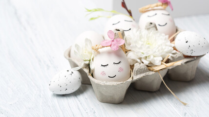 Easter holiday concept with cute handmade white eggs, tree branches, quail feathers and spring flowers on white wooden background.