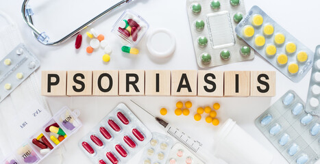 PSORIASIS word on wooden blocks on a desk. Medical concept with pills, vitamins, stethoscope and syringe on the background.
