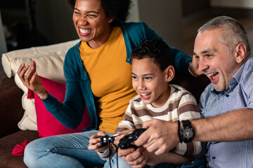 Smiling mixed race family enjoying time at home sitting on sofa playing video games.