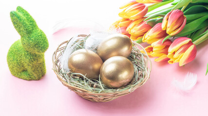 Easter Golden eggs in basket with spring tulips, white feathers on pastel pink background in Happy Easter decoration. Spring holiday concept.