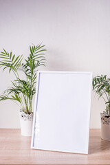Portrait white picture frame mockup on wooden table. Modern  vases with palms. White wall background. Scandinavian interior. Vertical