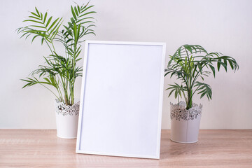 Portrait white picture frame mockup on wooden table. Modern  vases with palms. White wall background. Scandinavian interior. Vertical