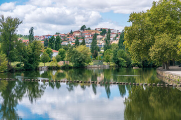 Fototapeta na wymiar Tamega River, calm water, leisure place, stone pass over the river. Chaves cityscape with leafy trees. Relaxation landscape.