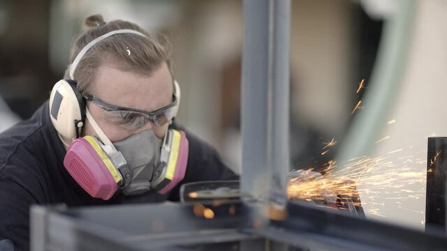 Male metal worker in respirator cutting metal construction with angle grinder