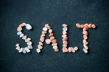 Word salt has written from crystals of Himalayan pink salt on black background.