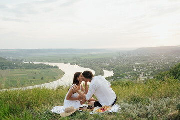 Naklejka na ściany i meble Happy young couple kissing and having picnic outdoors on summer day.