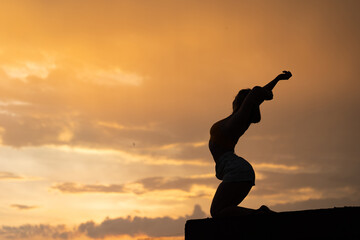 Fototapeta premium Flexible girl doing exercise on sky background during dramatic sunset