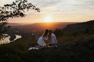 Happy young couple enjoying picnic on the hill. Sunset over hill in the background. Romance, dating...