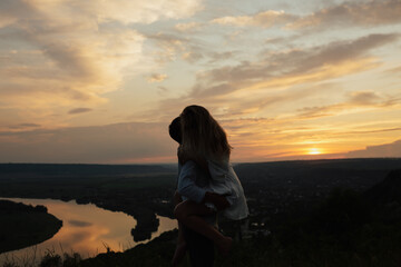 Silhouette of passionate couple with gorgeous sunset sky on background. Couple is kissing and hugging.