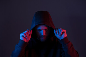 a man illuminated with colored neon lights puts on a hoodie