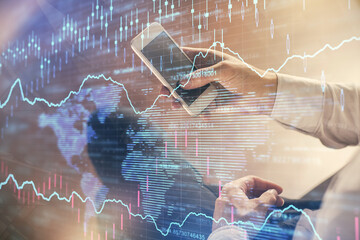 Double exposure of man's hands holding and using a digital device and forex graph drawing. Financial market concept.