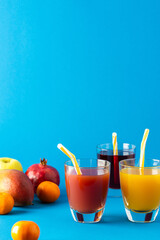 Delicious sweet citrus, mango and pomegranate juices in glasses and ripe fruits on a blue background