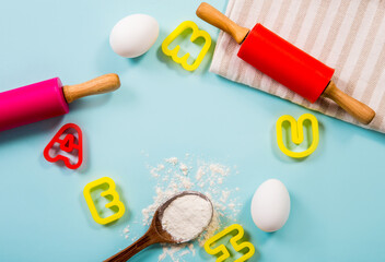 Fun cooking class for kids border concept lot of room for text. Eggs, flour, rolling pins, letter shape cookie cutters on light blue background, studio shot.