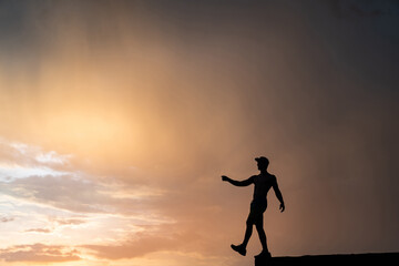 Muscular man stepping from the edge during dramatic sunset. Concept of choice and courage