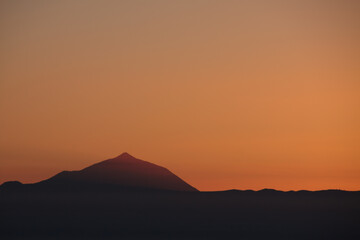 Silhouette of the Teide volcano backlit at sunset seen from Gran Canaria in warm orange tones