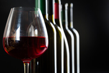 several different bottles of wine and a glass with red wine on a dark glossy background.